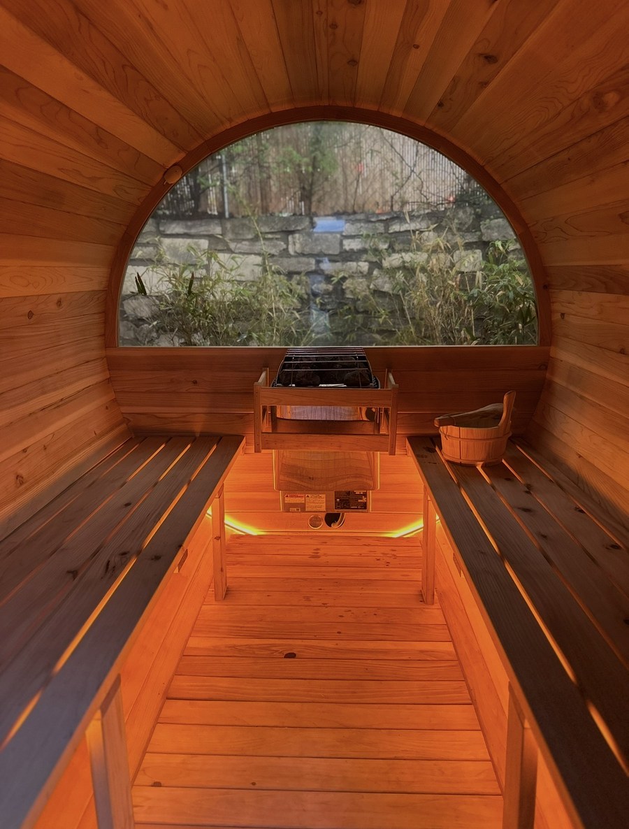 Inside the barrel sauna — cedar benches, heater and an arched window