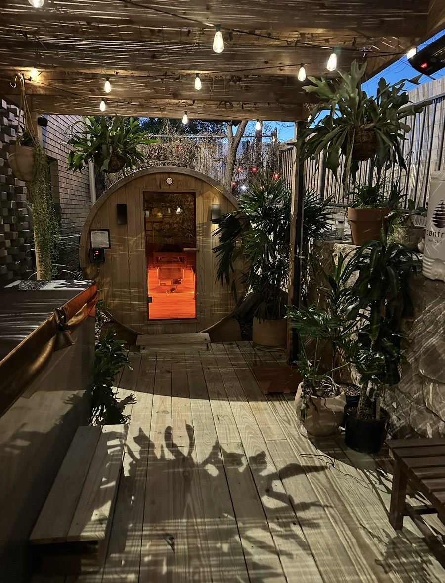 The barrel sauna glowing at dusk under string lights in the Garden